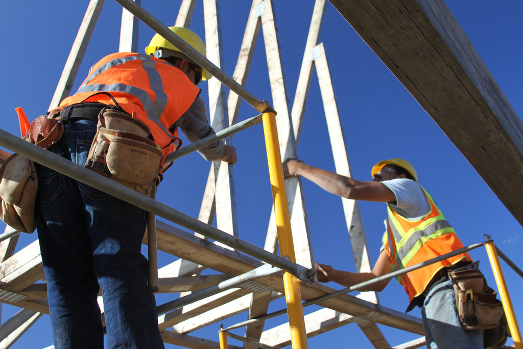 Two construction workers stand on scaffolding and work on building a wood frame.